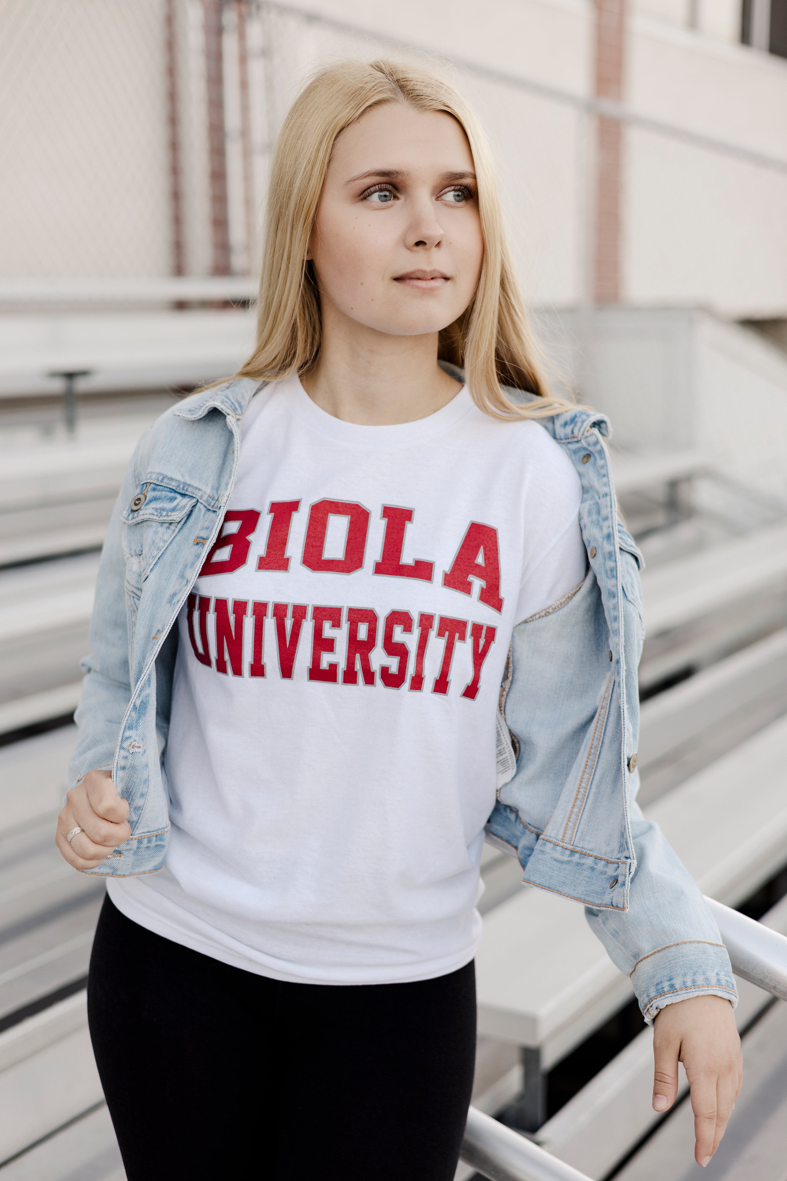 Woman wearing a white sweatshirt with 'Biola University' text, standing on bleachers outdoors.