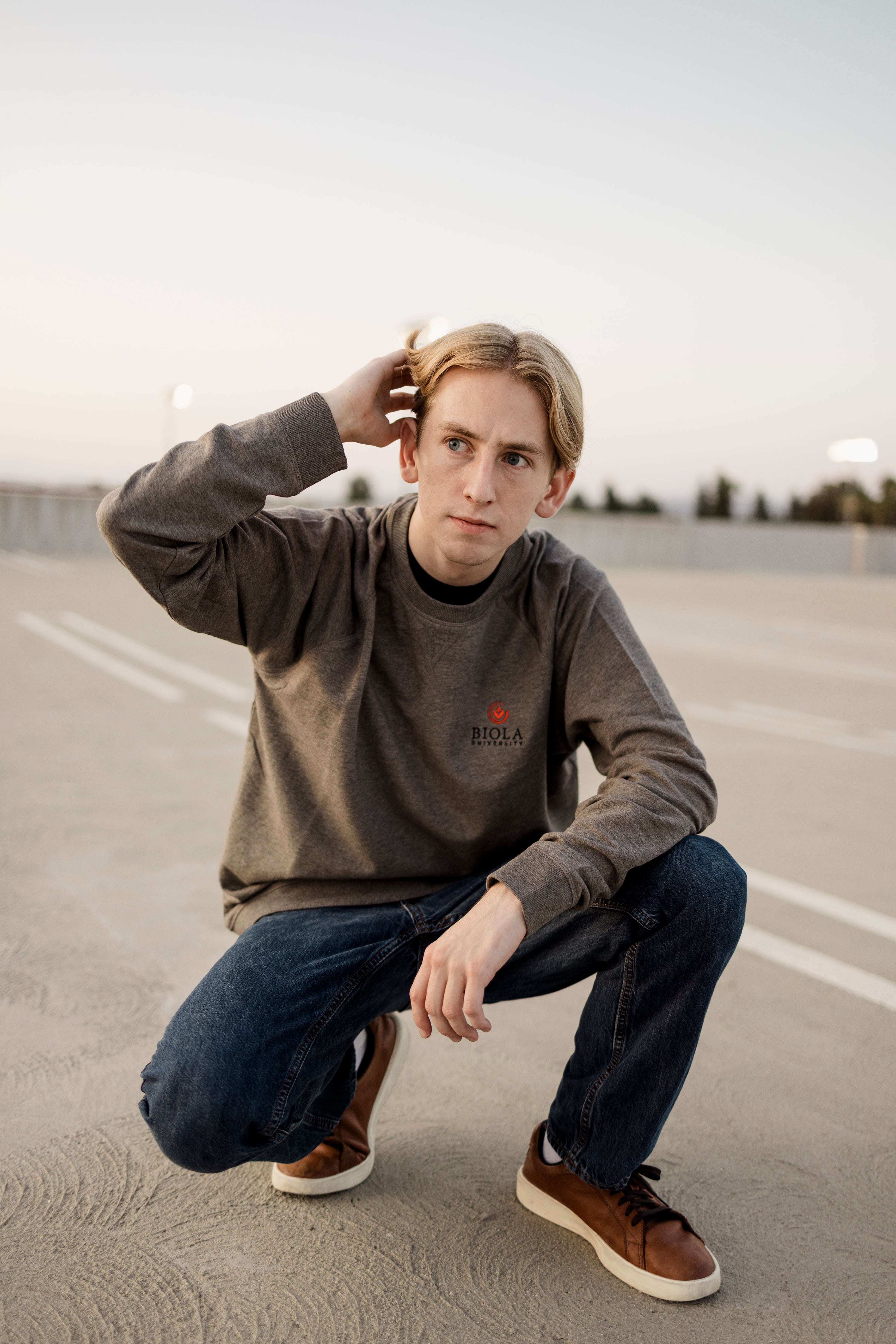 Man wearing a gray sweatshirt with a Biola logo, posing in a parking lot.
