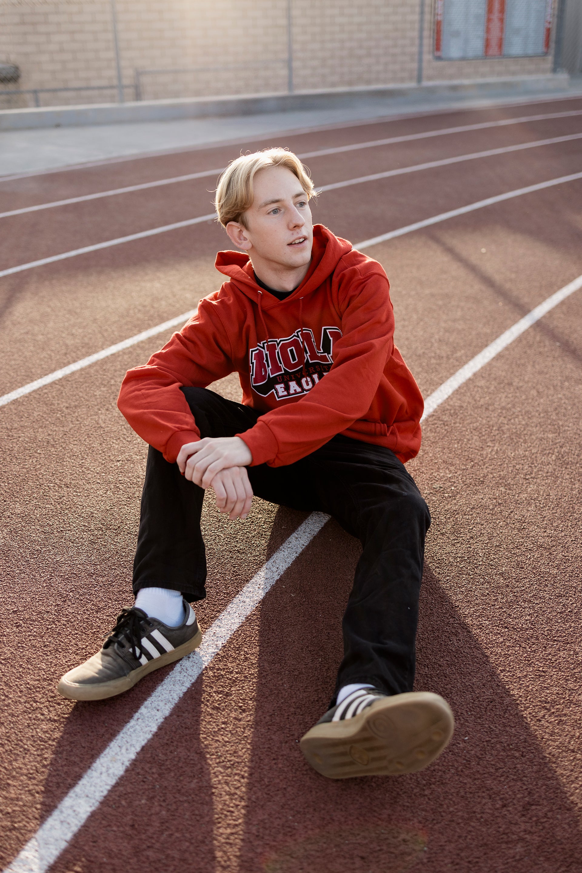 Man wearing a red hoodie sitting on a running track
