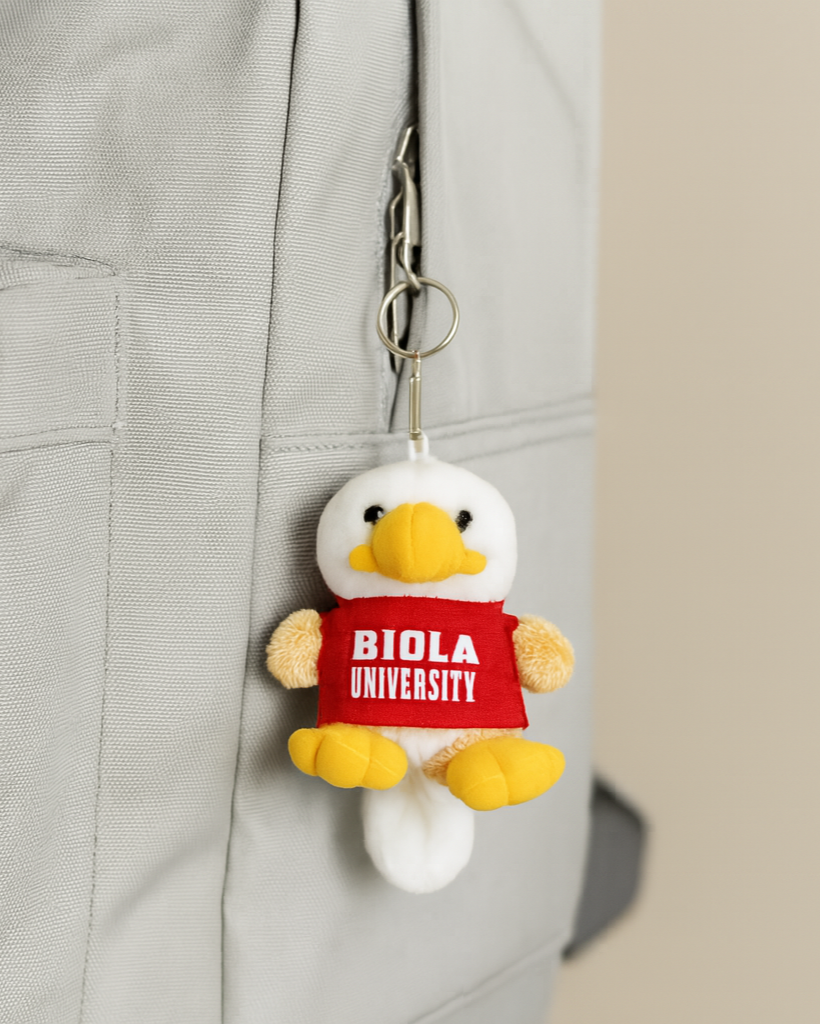 Plush duck keychain with 'Biola University' tag attached to a backpack.